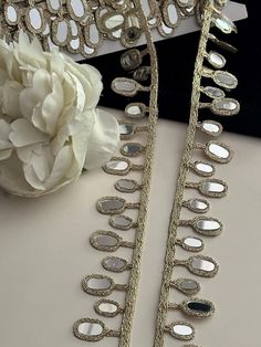 two pieces of jewelry sitting on top of a table next to a white flower and a pair of scissors