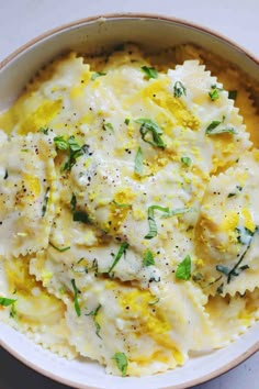 a white bowl filled with pasta covered in cheese and herbs on top of a table