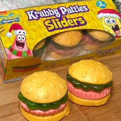 two toy hamburgers sitting on top of a wooden table next to a box of krabby patties sliders