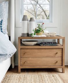 a nightstand with two vases on top of it next to a bed in a bedroom