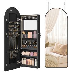 an open black jewelry cabinet next to a white couch and window with drapes on the windowsill