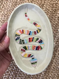 a hand holding a white bowl with colorful glass snakes on it