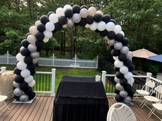 a black and white balloon arch is set up on a deck for an outdoor party