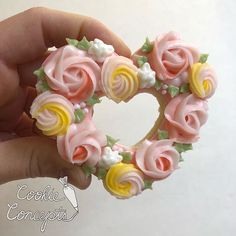 a hand holding a pink and yellow heart shaped pastry with flowers on it's side