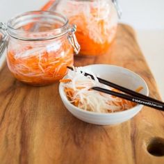 two jars filled with food sitting on top of a wooden table next to chopsticks