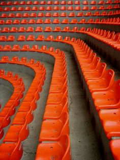 rows of orange plastic seats in an empty stadium or sports arena, with no one sitting at the stands