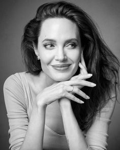 a black and white photo of a woman with her hands on her chin, smiling