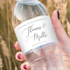 a person holding a bottle of water in front of some tall grass and flowers with the words welcome to the wedding of thomas and miles written on it