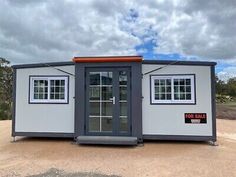 a portable home made out of shipping containers in the middle of a dirt lot with a door and windows