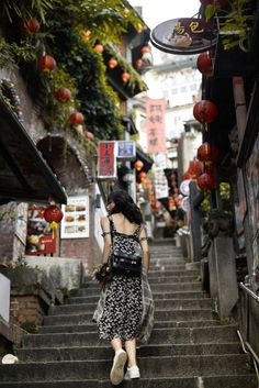 a woman walking up some steps in an alley way with lanterns hanging above her head