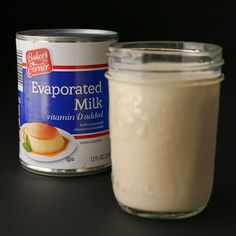 a glass jar filled with milk next to a can of food on a black surface