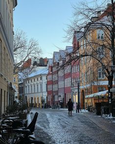 people walking down a cobblestone street in the winter with snow on the ground