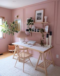 a room with pink walls and wooden floors has a desk, chair, potted plant on the far wall