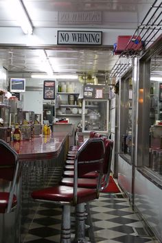 there are many red chairs at the bar in this diner's dining room that is empty