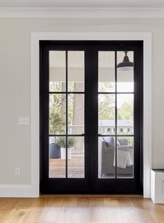 an empty room with two black doors and white walls, hardwood flooring, and large windows