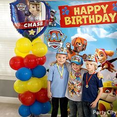 two boys standing next to each other in front of a happy birthday sign and balloons