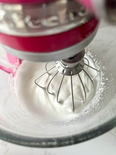 a close up of a mixer in a glass bowl with white powder on it and pink handle