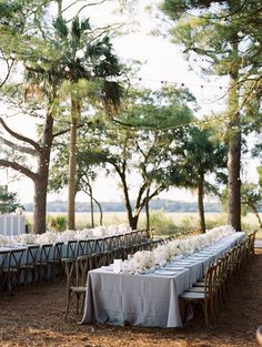 a long table is set up with white flowers and place settings for an outdoor wedding