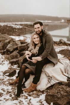 a man and woman are sitting on rocks in the snow with their arms around each other