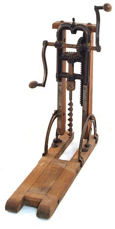 an old wooden machine with metal parts on it's legs and wheels, sitting on a white surface