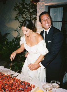 a man and woman are cutting into a cake with fruit on the table in front of them