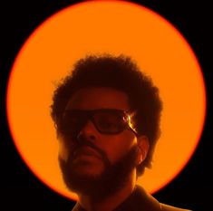 a man with sunglasses and a beard standing in front of an orange sun