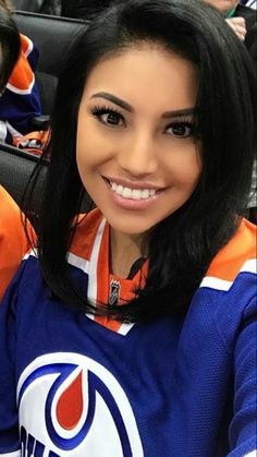 a woman with long black hair and an edmonton oilers jersey is smiling for the camera