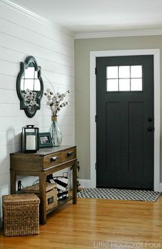 a hallway with a black door and wooden flooring next to a mirror on the wall