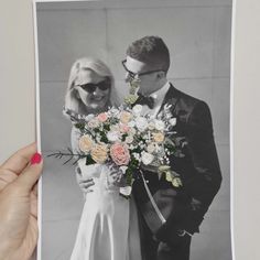 a man and woman holding a bouquet of flowers in front of a photo on the wall