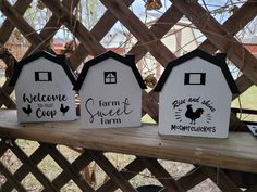 three birdhouses with farm signs on them sitting on a wooden bench in front of a fence