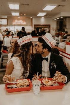 a man and woman sitting at a table with food in trays on their heads