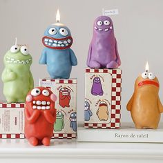 three candles that look like monsters sitting on top of boxes with cards in front of them