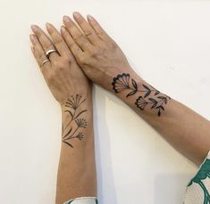 two hands are holding each other with tattoos on their arms and wrist, one has a flower tattoo on its left arm