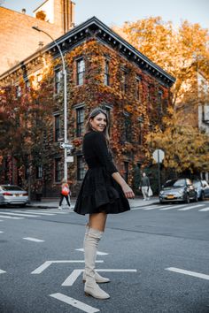 a woman standing on the street in front of an old brick building wearing knee high boots