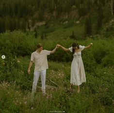 a man and woman holding hands while standing in a field with wildflowers behind them