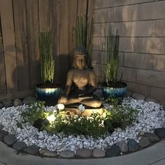 a buddha statue sitting in the middle of a garden with plants and rocks around it