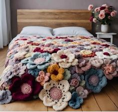 a crocheted blanket is laying on the floor in front of a bed with flowers