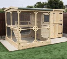 a large wooden chicken coop with doors open on top of grass covered ground next to a fence