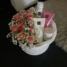 a bouquet of pink roses in a white basket on a black table next to a candle