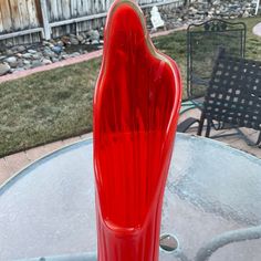 a red vase sitting on top of a glass table next to a black metal chair