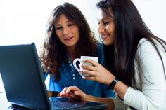 two women are looking at a laptop screen and holding a coffee mug in their hands