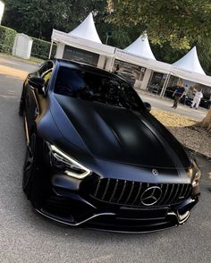 a black sports car parked in front of a white tent on the side of a road