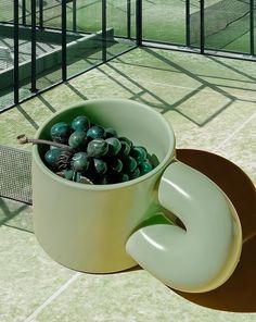 a white cup filled with green marbles on top of a tennis court next to a net