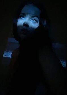 a woman in the dark looking up at something on her screen with blue light coming from behind her