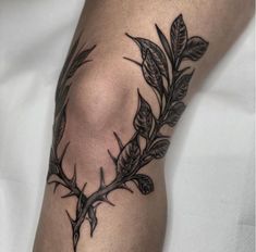 a black and white photo of a tattoo on someone's leg with leaves around it