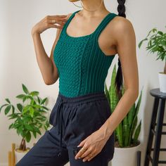 a woman with her hands on her hips wearing black pants and a green tank top