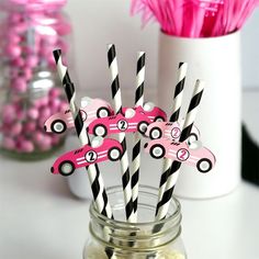 pink and black paper cars are in a mason jar with striped straws on top