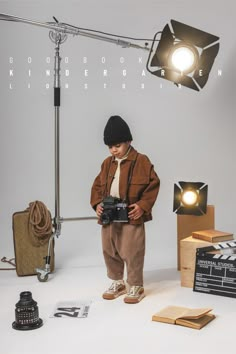 a young boy is holding a camera in front of a light and some other items