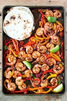 a pan filled with shrimp and vegetables next to a tortilla