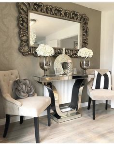 two chairs and a table in front of a mirror with vases on the side